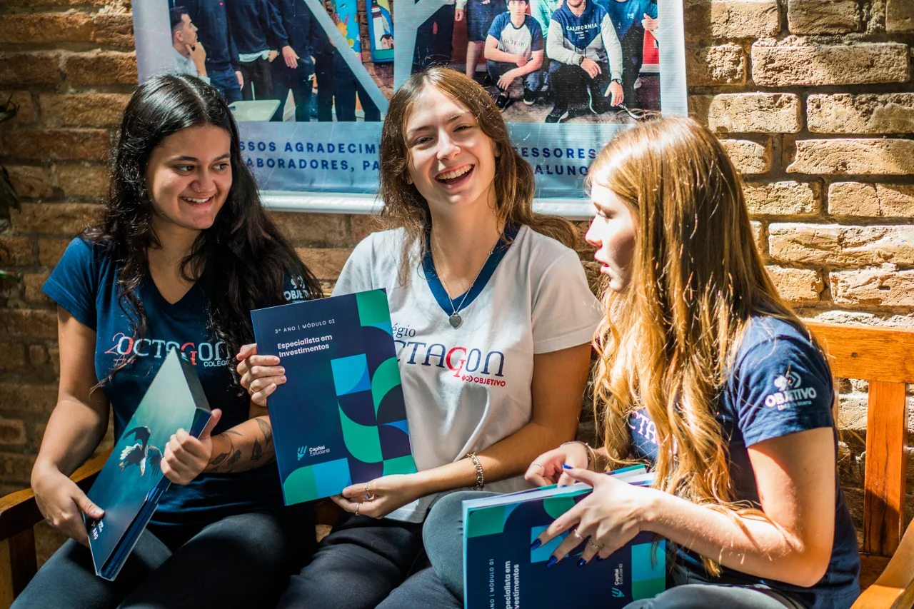Três alunas do Colégio Octagon conversando e sorrindo com seus livros